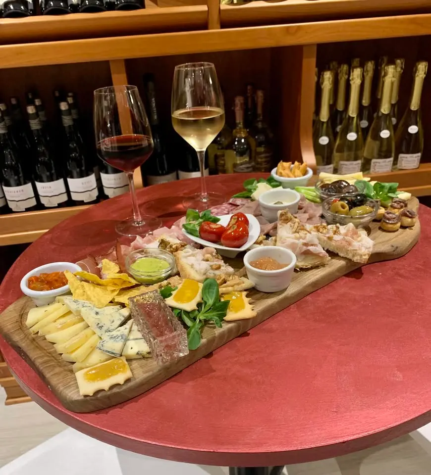 Tagliere di salumi e formaggi con due calici sul tavolino di diVINUM